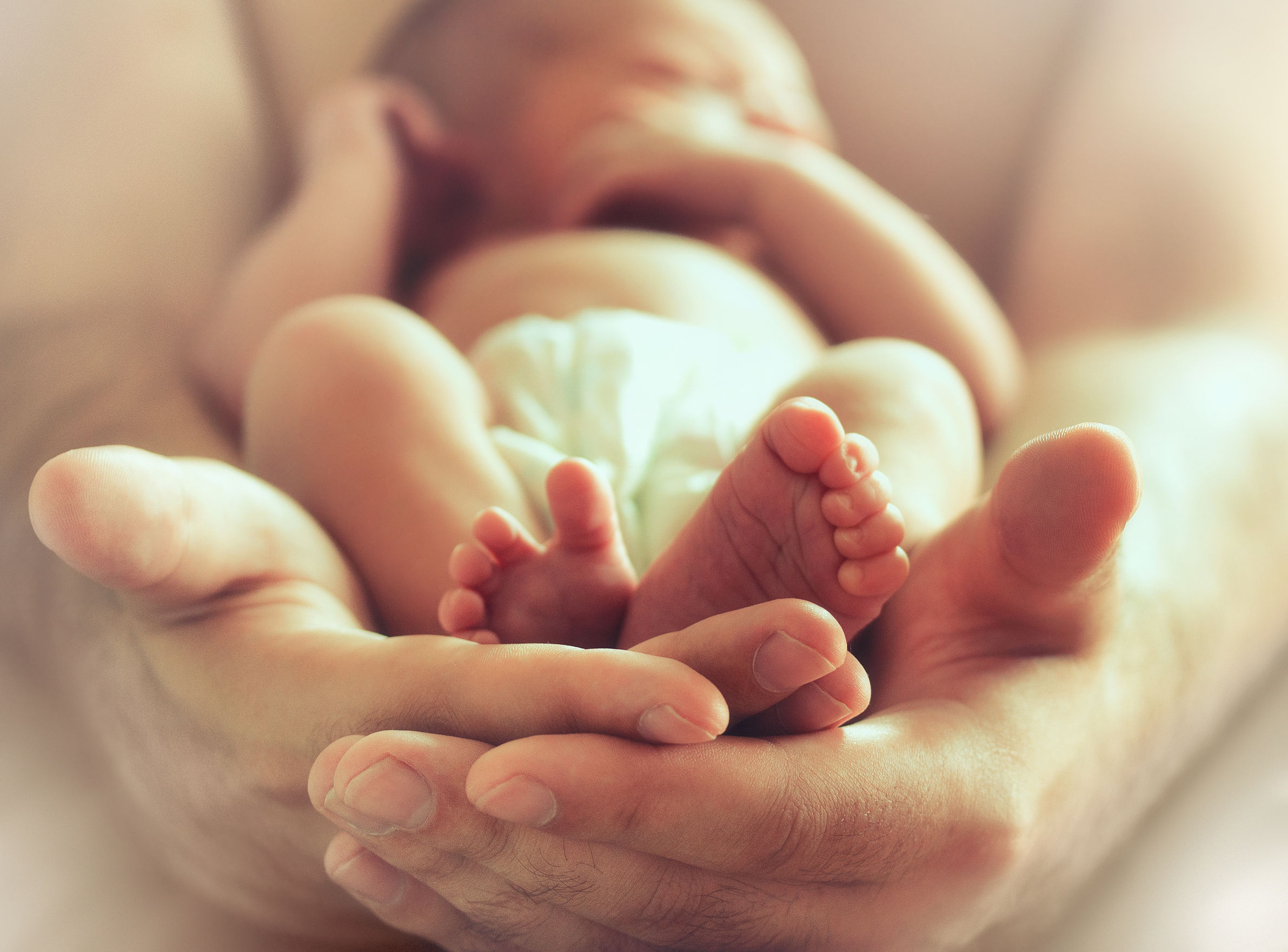 strong male hands holding sleeping newborn baby, photo with soft blur effect